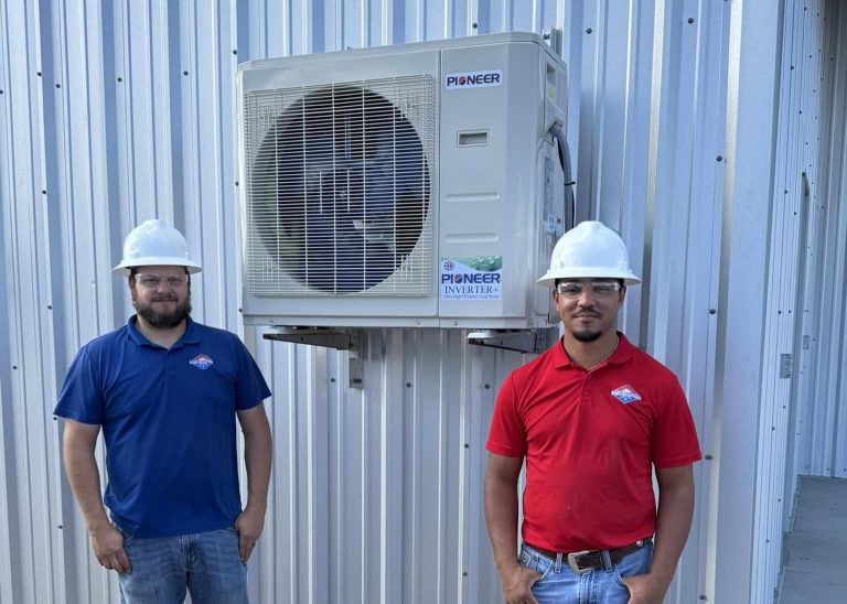 Two team members in front of an AC unit